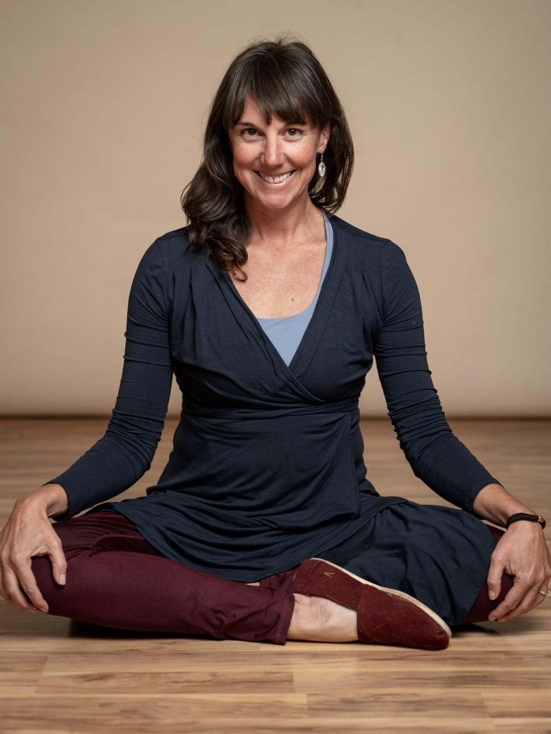 Allison, a holistic nurse coach, sitting cross-legged on a wooden floor and smiling